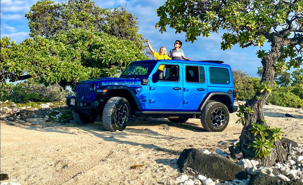 Blue Jeep Wrangler Rubicon on a sandy beach in Hawaii; kids sranding up through the open roof